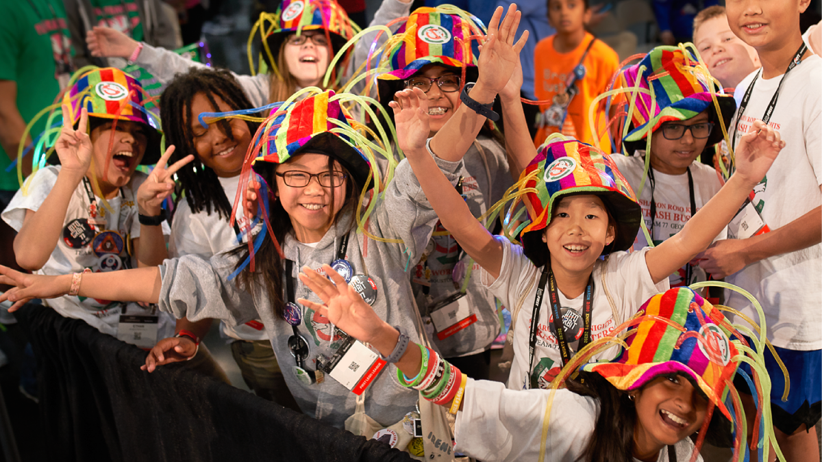 A group of children participating in FIRST LEGO League, smiling and waving at the camera